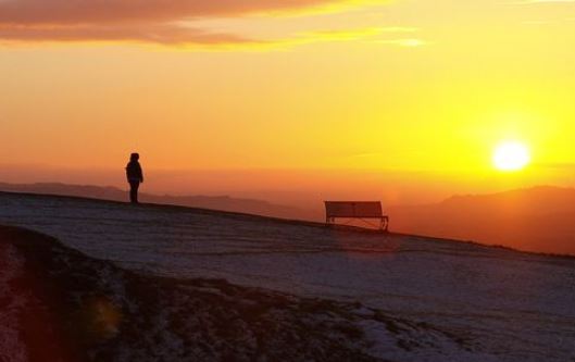 a setting sun with a single figure standing looking over the edge of a hill in Gloucestershire UK